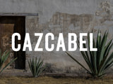 Cazcabel tequila wordmark against a faded white Mexican outdoor wall in daylight