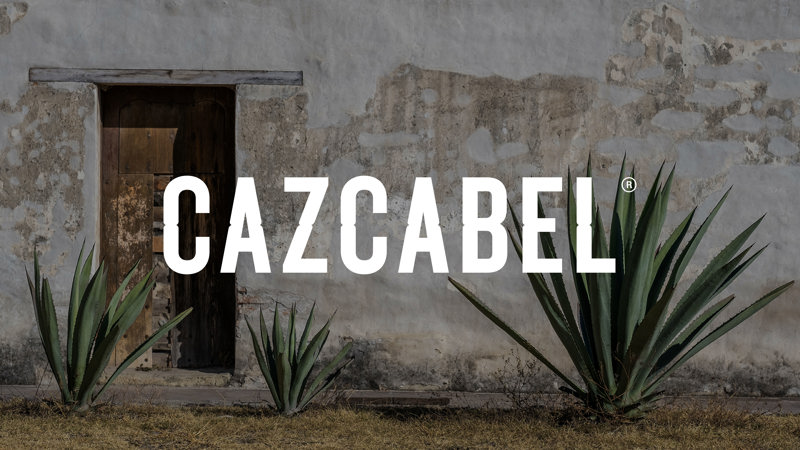 Cazcabel tequila wordmark against a faded white Mexican outdoor wall in daylight