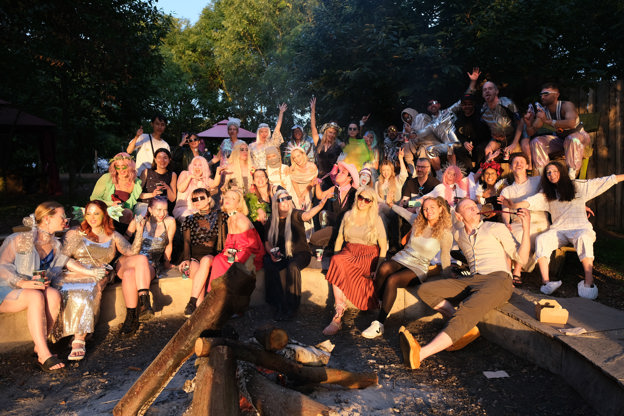 A group of smiling people sit in a woodland as the sun goes down. They are happy and dressed in sci-fi fancy dress.
