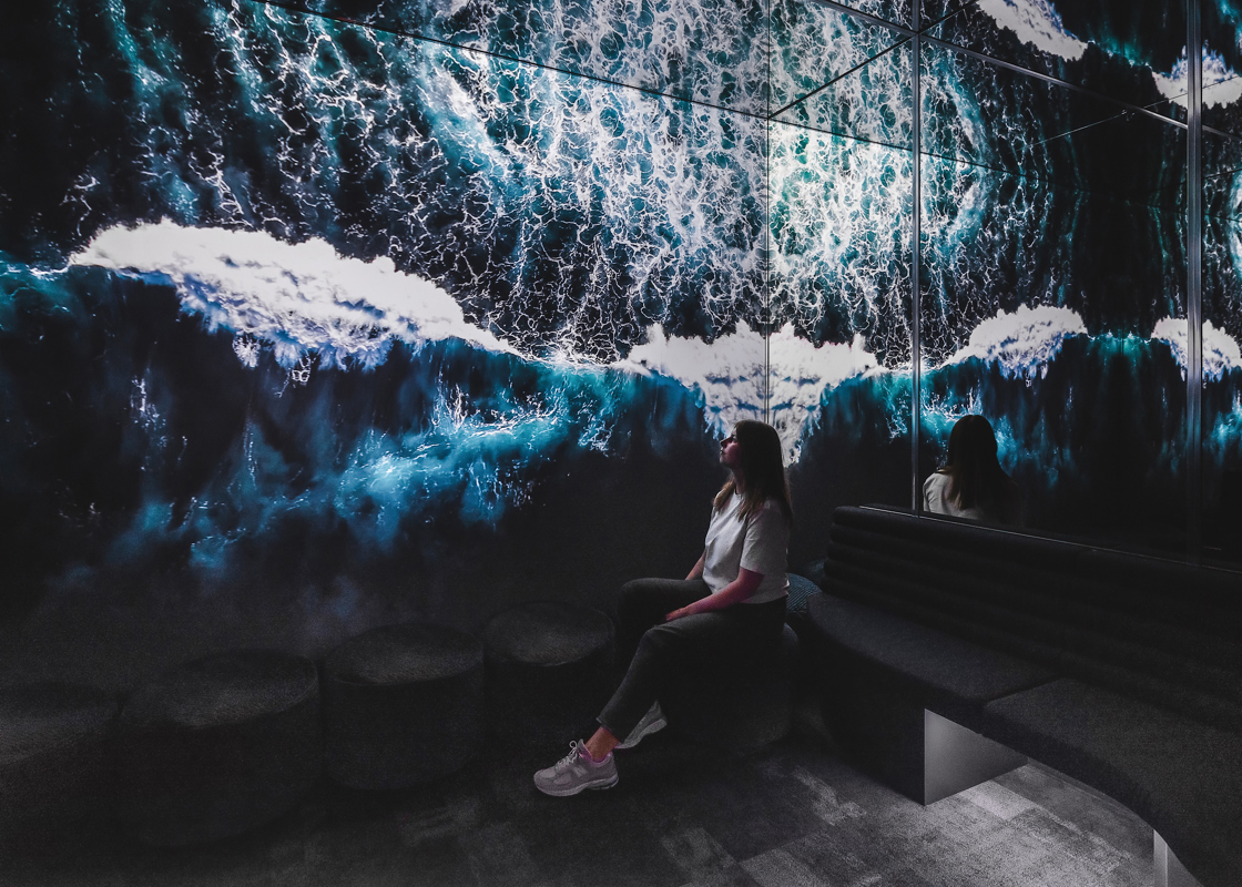 Woman sits peacefully in a room with large digital screen and seascape image